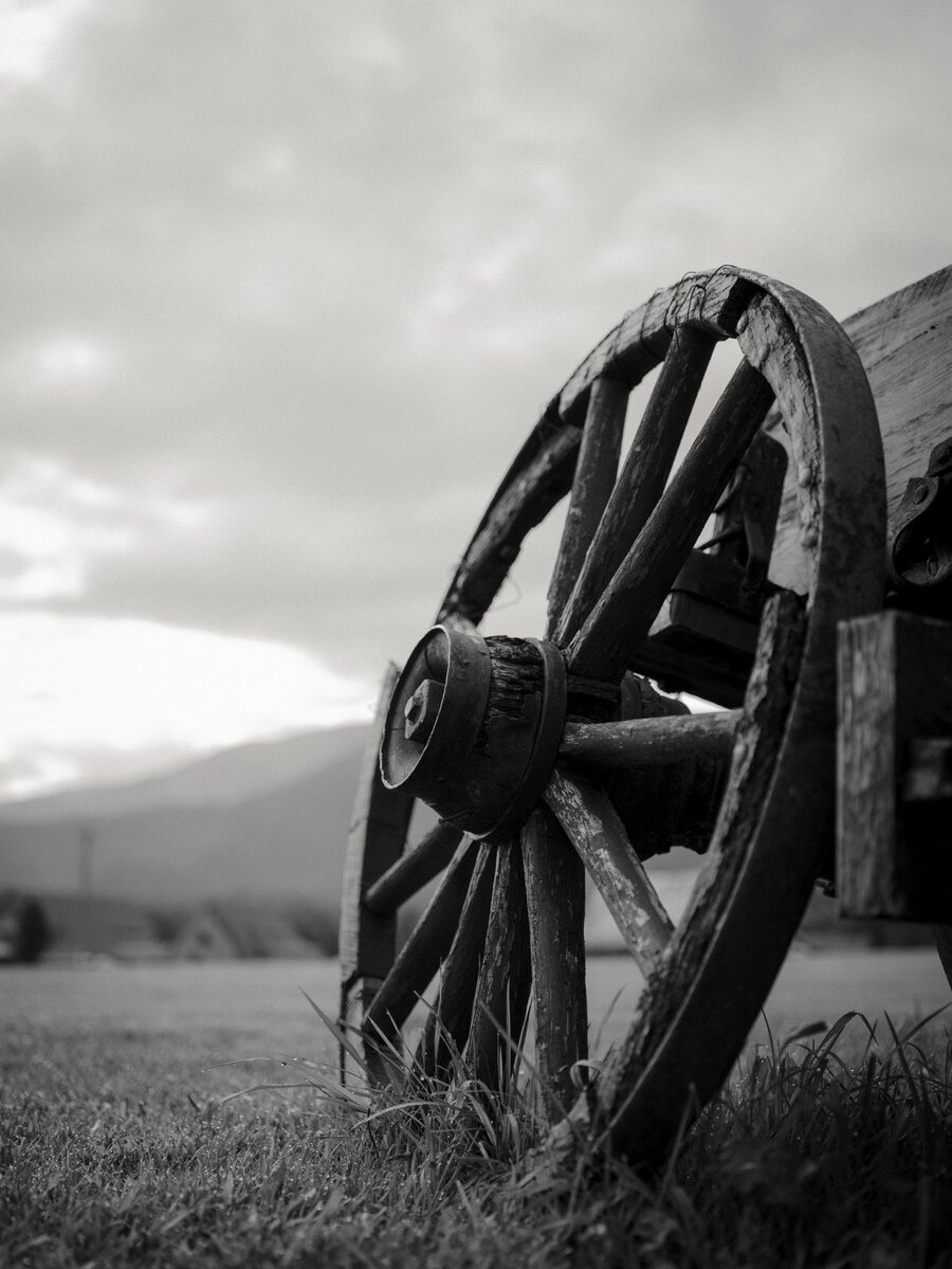 Black-and-white close-up photograph of a weathered wooden wagon wheel beneath an open sky
